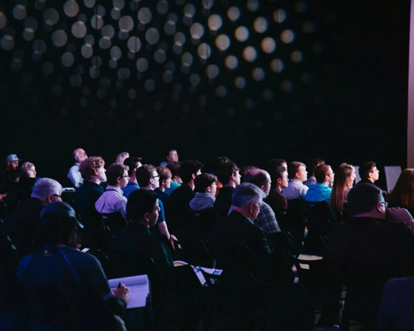 Publikum sitzt bei einer Veranstaltung im abgedunkelten Saal